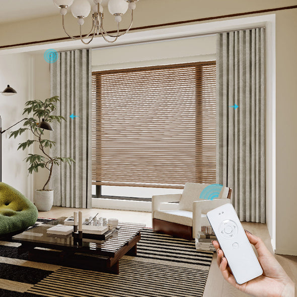 Living room with a hand holding a blinds remote control and a window with smart blinds