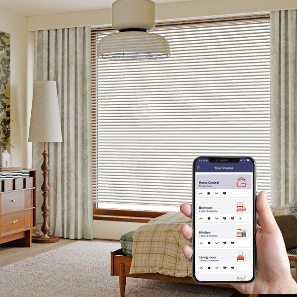 Hand holding a smartphone with smart blinds app control in a bedroom 